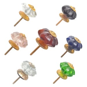 May include: A collection of seven decorative cabinet knobs. Each knob features a flower-shaped, faceted glass design in various colors, including clear, black, pink, red, blue, and green. The knobs have a gold-colored metal base and screw.