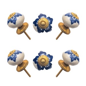May include: Six ceramic cabinet knobs. The knobs have a white base with blue floral designs and gold accents. Each knob has a gold-colored metal base and screw for installation. The knobs are designed for furniture or cabinet doors.