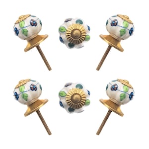 May include: Six decorative cabinet knobs. The knobs have a white base with blue and green floral designs. The center knob has a gold-colored sunflower design. The knobs have gold-colored bases and threaded rods.