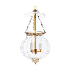 May include: Clear glass hanging lantern with a gold-colored metal frame and accents. The lantern has a round, ribbed glass body, a small clear glass top, and a decorative bottom. Two small, white candle-shaped lights are visible inside.