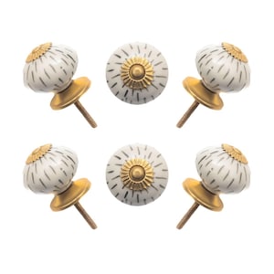 May include: Six decorative cabinet knobs. The knobs have a white base with a black dotted pattern and a gold-colored metal base and screw. The top of the knob has a gold-colored floral design.