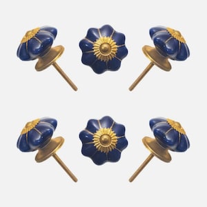 May include: Six navy blue flower-shaped cabinet knobs with gold-colored accents. Each knob has a brass-colored base and a threaded screw for installation. The knobs are arranged in a circular pattern against a white background.