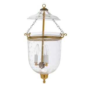 May include: Clear glass lantern with a brass frame and accents. The lantern features a star pattern etched into the glass and is suspended by a chain. The lantern has two light bulbs inside. The overall design is elegant and decorative.