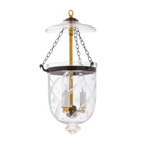 May include: Clear glass hanging lantern with etched floral and star patterns. The lantern features two light bulbs, a brass rod, and a black metal band. It is suspended by chains and has a clear glass top.