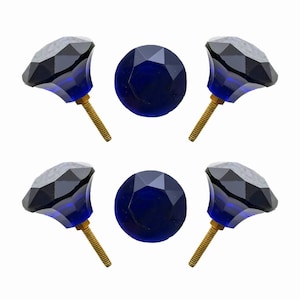May include: A set of four faceted blue glass cabinet knobs with brass screws and two matching flat, round glass pieces. The knobs have a dark blue, gem-like appearance, and the screws are gold-colored.