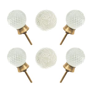 May include: Five clear glass cabinet knobs with a diamond pattern and brass hardware. The knobs are spherical and have a vintage aesthetic, suitable for furniture restoration or home decor projects.