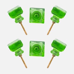 May include: A collection of five green glass cabinet knobs. Two square knobs and three knobs with a faceted top and a brass screw. The knobs are a vibrant green color and are set against a white background.