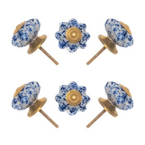 May include: Six decorative cabinet knobs. The knobs have a white and blue speckled floral design with a gold-colored base and screw. The knobs are arranged in a circular pattern against a white background.