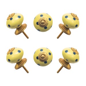 May include: Six yellow ceramic cabinet knobs with blue polka dots and gold-colored hardware. Each knob has a decorative gold flower-like accent. The knobs are designed for furniture and home decor.