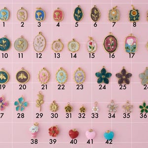 A collection of gold plated stainless steel charms. Charms include flowers, bees, and hearts. Charms are laid out on a pink background with identifying numbers.