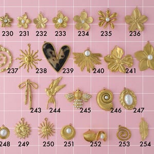 A collection of gold plated stainless steel big charms. Charms include flowers, hearts, geometric shapes, and pearls. Charms are laid out on a pink background with identifying numbers.