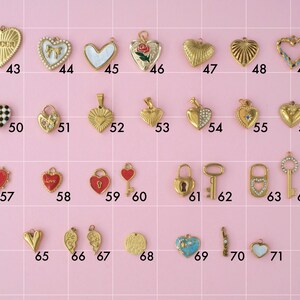 A collection of gold plated stainless steel charms in "love" theme. Charms include hearts, key and locks. Charms are laid out on a pink background with identifying numbers.