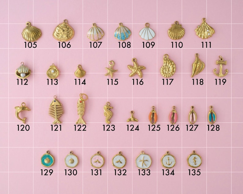 A collection of gold plated stainless steel charms in ocean theme. Charms include shells, pearls, anchors, fish, dolphin, starfish, and seahorses. Charms are laid out on a pink background with identifying numbers.