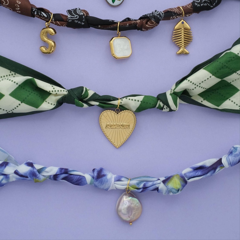 Scarf necklaces with floral and geometric patterns. Scarves have charms attached to them that include the letter "S", pears, gold heart, and a fish.