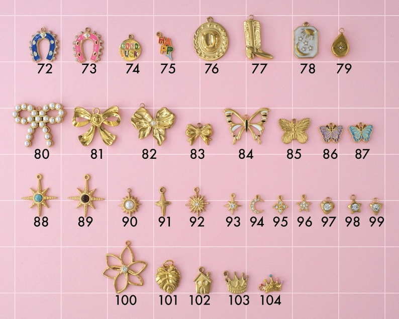 A collection of gold plated stainless steel charms. Charms include lucky charms, cowboy boot and hat, bows, butterflies, stars, moon, monstera leaf, and king crowns. Charms are laid out on a pink background with identifying numbers.