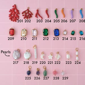 A collection of gold plated stainless steel charms. Charms include hot peppers, gemstones, and pearls. Charms are laid out on a pink background with identifying numbers.