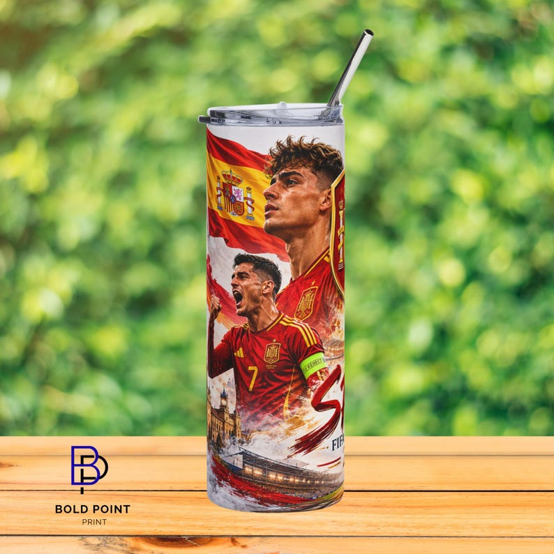 K&ouml;nnte beinhalten: Ein zylindrischer Edelstahlbecher mit einem Grafikdruck der spanischen Fu&szlig;ballnationalmannschaft, der zwei Spieler in roten Trikots, die spanische Flagge und ein Stadion zeigt. Der Becher hat einen transparenten Deckel und einen Metallstrohhalm.