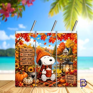 Op de afbeelding: Een cilindrische beker met rietje voorzien van een herfstachtige illustratie van Snoopy met een oranje gebreide muts en sjaal, die een mok vasthoudt met de tekst Hello Fall. Het ontwerp bevat een houten bord met tekst, pompoenen en een lantaarn.
