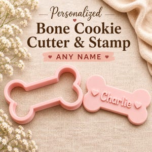Może przedstawiać: Jasnoróżowa foremka do ciastek w kształcie kości oraz pasująca pieczątka z imieniem Charlie i dwoma małymi sercami. Tekst Personalized Bone Cookie Cutter & Stamp ANY NAME znajduje się nad przedmiotami w ciemnobrązowym i różowym kolorze.