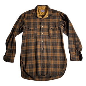 May include: A long-sleeve button-down shirt featuring a brown and dark grey plaid pattern. The shirt has a pointed collar with a mustard yellow inner lining, two chest pockets with buttoned flaps, and a curved hemline. A Pendleton label is visible.