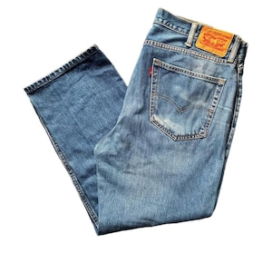 May include: Light blue denim jeans with a classic five-pocket design. The jeans feature a faded wash and a red Levi's tag on the back pocket. The jeans have a straight leg cut and are made of durable denim.