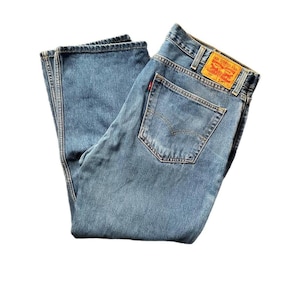 Pode incluir: Jeans de ganga azul claro com um design clássico de cinco bolsos. Os jeans apresentam uma etiqueta vermelha Levi's no bolso traseiro e uma pequena etiqueta vermelha. Os jeans estão dobrados e parecem não usados.