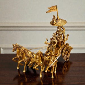May include: A gold-colored metal sculpture depicting a chariot pulled by four horses. Two figures are seated in the chariot, and a flag is mounted above. The sculpture is highly detailed and ornate.