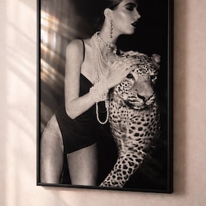 May include: Black and white framed print featuring a woman in a black dress and pearl jewelry, gently touching a leopard. The image has a vintage, glamorous aesthetic, with dramatic lighting and a focus on texture.