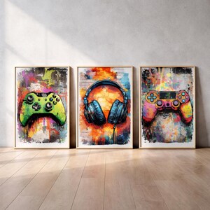 Op de afbeelding: Drie ingelijste kunstprints met gamingthema's. Eén print toont een groene gamecontroller, een andere een blauwe koptelefoon en de derde een kleurrijke gamecontroller. Elke print heeft een kleurrijke, abstracte achtergrond.