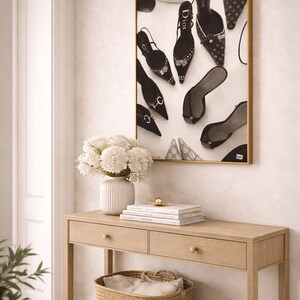 Puede incluir: Una obra de arte enmarcada con una colecci&oacute;n de zapatos de tac&oacute;n alto de varios estilos y marcas. Debajo de la obra hay una consola de madera clara con dos cajones y una cesta tejida. Un jarr&oacute;n blanco con flores blancas est&aacute; sobre la mesa.