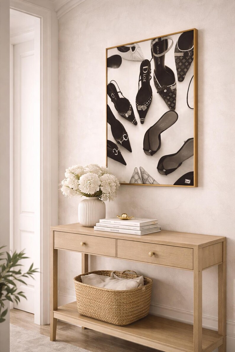 Puede incluir: Una obra de arte enmarcada con una colecci&oacute;n de zapatos de tac&oacute;n alto de varios estilos y marcas. Debajo de la obra hay una consola de madera clara con dos cajones y una cesta tejida. Un jarr&oacute;n blanco con flores blancas est&aacute; sobre la mesa.