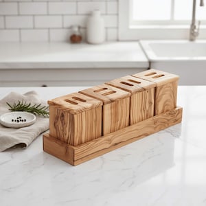 Peut inclure: Un ensemble de porte-ustensiles en bois avec quatre compartiments carrés et une base rectangulaire. Chaque compartiment a une ouverture rectangulaire sur le dessus. Le grain du bois est visible, et l'ensemble est présenté sur un comptoir blanc.
