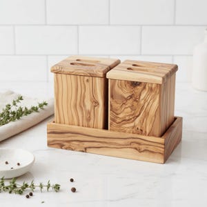Peut inclure: Deux boîtes à épices en bois d'olivier avec couvercles, posées sur un plateau assorti. Les boîtes et le plateau présentent un veinage naturel du bois. Chaque couvercle de boîte comporte une fente. L'ensemble est conçu pour la cuisine.