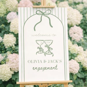 Puede incluir: Un caballete de madera exhibe un letrero de bienvenida para el compromiso de Olivia y Jack. El letrero presenta un lazo verde, dos copas de champán y texto sobre un fondo blanco con rayas verdes. Flores blancas y rosas rodean el letrero.