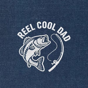 May include: A navy blue fabric with a white embroidered design. The design features a fish, fishing rod, and the text "REEL COOL DAD" in a circular arrangement. The fish is detailed with scales and fins.