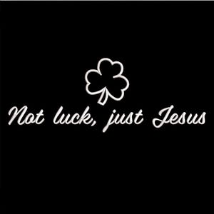May include: Black background with white text and a white shamrock. The text reads "Not luck, just Jesus". The shamrock is above the text. The text and shamrock are in a cursive font.