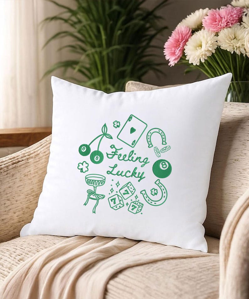 Pode incluir: Almofada quadrada branca com um gr&aacute;fico verde de &iacute;cones com tema de cassino, incluindo cerejas, uma carta de baralho, dados, uma ferradura e uma bola oito. As palavras "Feeling Lucky" s&atilde;o escritas em uma fonte de script. A almofada est&aacute; em uma superf&iacute;cie bege.