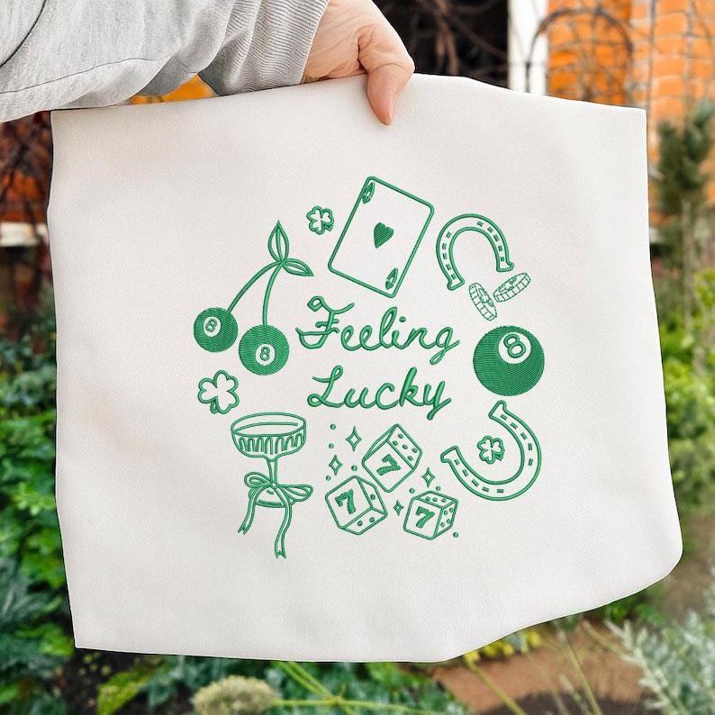 Pode incluir: Uma sacola branca com um design verde com o texto "Feeling Lucky" e v&aacute;rios s&iacute;mbolos da sorte, incluindo uma carta de baralho, dados, cerejas, uma ferradura e uma bola de bilhar.