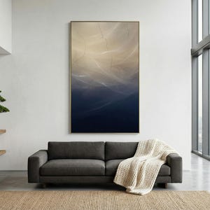 May include: A modern living room featuring a dark gray sofa with a cream-colored throw blanket, a large abstract painting with blue and beige tones, and a bonsai tree on a wooden shelf. A large window offers a city view.