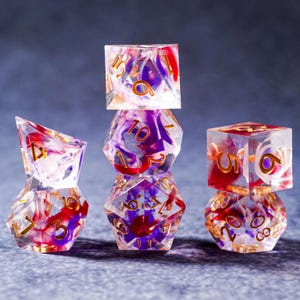 May include: A collection of clear, multi-sided dice with red, purple, and gold accents. The dice are stacked and arranged to showcase their various shapes and the intricate patterns within. Ideal for tabletop gaming.