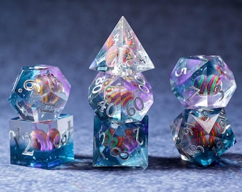 May include: A set of clear, multi-sided dice with colorful, swirled inclusions. The dice are transparent with silver numbering and are arranged on a dark blue background. The inclusions feature shades of purple, red, and yellow.