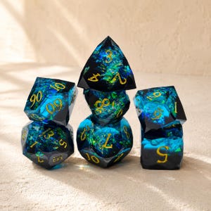 Può includere: Un set di sette dadi poliedrici per giochi da tavolo. I dadi sono un mix di nero e blu traslucido con numeri dorati. L'interno dei dadi presenta un motivo a vortice, simile a una galassia, con sfumature verdi e blu.