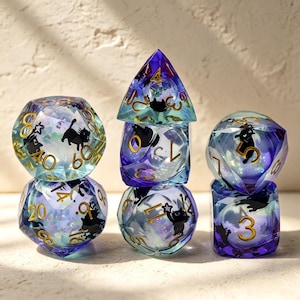 Peut inclure: Un ensemble de sept dés polyédriques en résine translucide avec un dégradé bleu et violet. Chaque dé présente des silhouettes de chats noirs incrustées et des chiffres dorés. Les dés sont disposés en trois piles, montrant diverses formes géométriques dont d20, d12, d10, d8, d6 et d4, avec des paillettes irisées à l'intérieur.