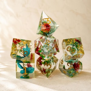 May include: A set of seven polyhedral dice, each with a clear resin body. The dice are filled with colorful flowers and leaves, with gold-colored numbers. The dice are arranged in a stacked formation.