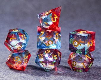 May include: A collection of colorful, gemstone-like dice. The dice are various shapes, including d6, d10, and d20. The dice are a mix of red, blue, and clear with gold numbering. The dice are stacked on top of each other.
