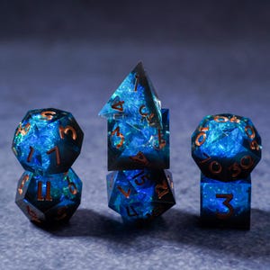 Può includere: Un set di sette dadi poliedrici per giochi da tavolo. I dadi sono di un blu intenso con un effetto scintillante simile a una galassia e numeri color rame. Il set include un D4, D6, D8, D10, D12, D20 e un dado percentuale.