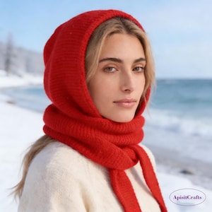 Peut inclure: Une femme porte un ensemble bonnet et écharpe en tricot rouge vif. Le bonnet encadre le visage et l'écharpe s'enroule autour du cou, avec de longues attaches. L'arrière-plan montre un paysage enneigé et un plan d'eau.