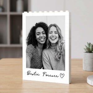 Könnte beinhalten: Ein weißer, rechteckiger Bilderrahmen aus ineinandergreifenden Kunststoff-Bausteinen. Der Rahmen zeigt ein schwarz-weißes Foto von zwei lächelnden Personen und trägt den Schriftzug Bestie Forever mit einem Herzsymbol.