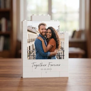 Könnte beinhalten: Ein weißer Baustein-Aufsteller mit einem Foto eines sich umarmenden Paares. Der Text Together Forever und das Datum 22.05.2023 sind unter dem Bild in Schwarz aufgedruckt, mit einem kleinen Herzsymbol ganz unten auf dem Baustein.