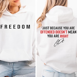 May include: White hoodie with the word "FREEDOM" printed in black on the front. The back of the hoodie features the quote "JUST BECAUSE YOU ARE OFFENDED DOESN'T MEAN YOU ARE RIGHT" in red and black text, with a signature.